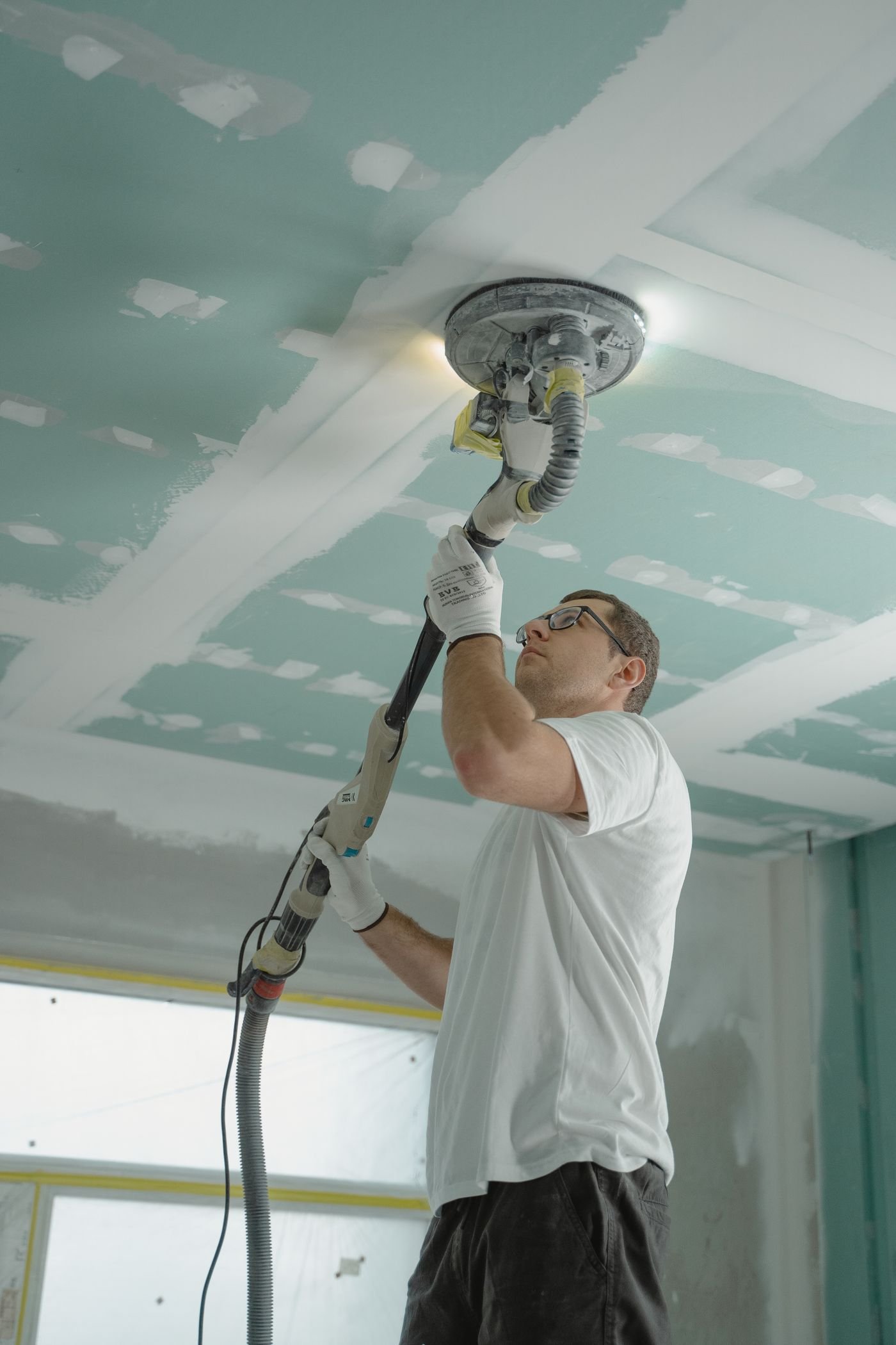 Technician sanding a repaired drywall ceiling after water damage